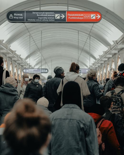 The image shows a group of pedestrians ascending a wide, grey stone staircase inside a busy train station, with some people wearing backpacks and casual clothing, and one man in a suit carrying a back